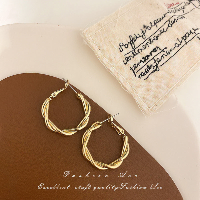 Twisted rope design gold hoop earrings on brown display