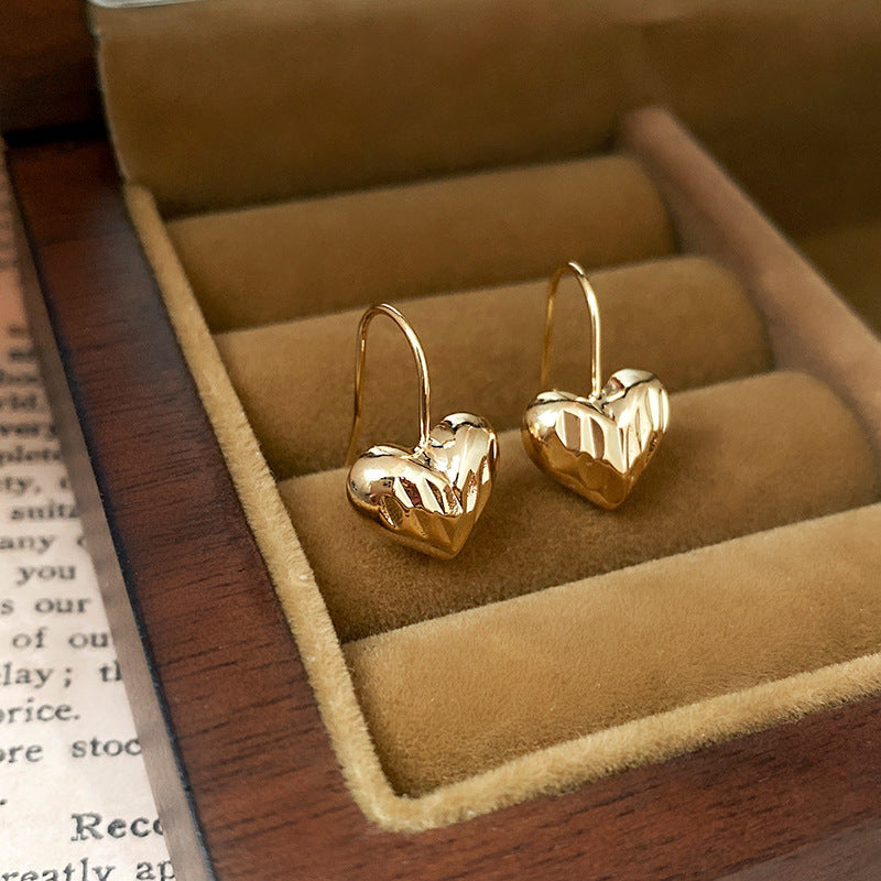 Sculptural heart-shaped gold hook earrings in jewelry box