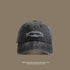 A dark gray washed cotton baseball cap with white 'San Francisco USA California' embroidery displayed against taupe background with travel text