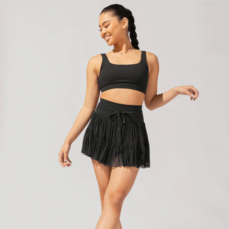 Model wearing black matching set with sports bra and tiered tennis skirt, showing playful movement pose