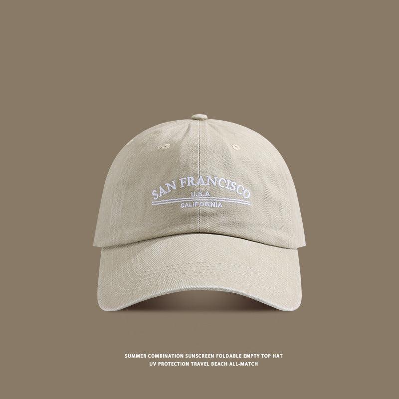 A beige washed cotton baseball cap with white 'San Francisco USA California' embroidery displayed against taupe background with UV protection text