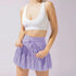 Lavender tennis skirt with ruffle tiers and drawstring waist, paired with white sports bra on light background