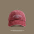 A brick red washed cotton baseball cap with white 'San Francisco USA California' embroidery displayed against taupe background with beach text