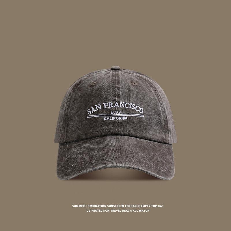 A charcoal gray washed cotton baseball cap with white 'San Francisco USA California' embroidery shown against taupe background with sun protection text