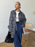 Navy blue plaid oversized shirt jacket paired with white top and navy sweatpants, modern minimalist outfit against white wall