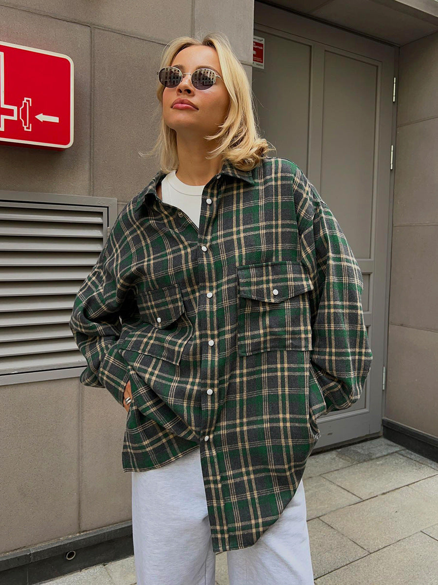 Forest green windowpane plaid shacket with white pants and oval sunglasses, urban casual style against industrial backdrop
