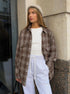 Brown plaid flannel shirt styled with gray beanie and white sweatpants, casual winter outfit against concrete wall