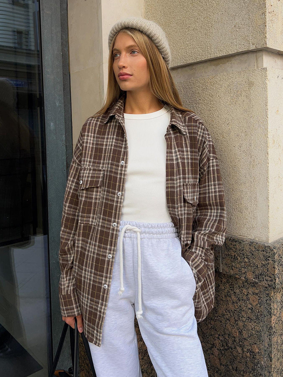 Brown plaid flannel shirt styled with gray beanie and white sweatpants, casual winter outfit against concrete wall