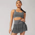 Model wearing gray matching workout set featuring sports bra and tiered tennis skirt against neutral backdrop