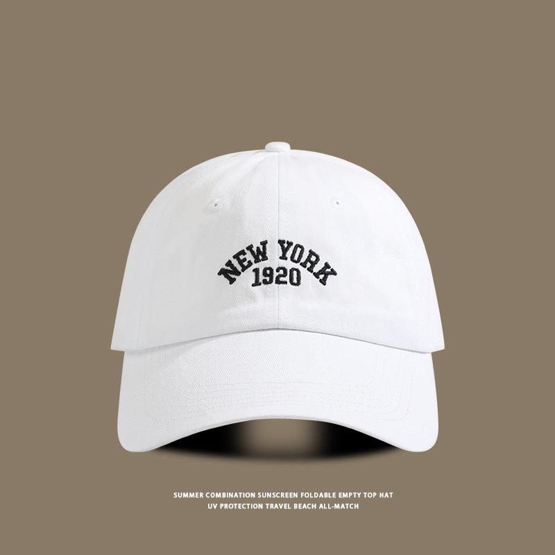 White baseball cap showcasing "New York 1920" embroidered in black, photographed against a muted brown backdrop