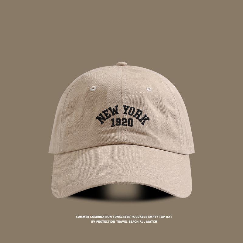 Beige baseball cap with "New York 1920" embroidered in black, displayed on a brown-toned background