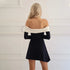 Back view of a black mini dress with white off-shoulder band and fitted sleeves against a white wall