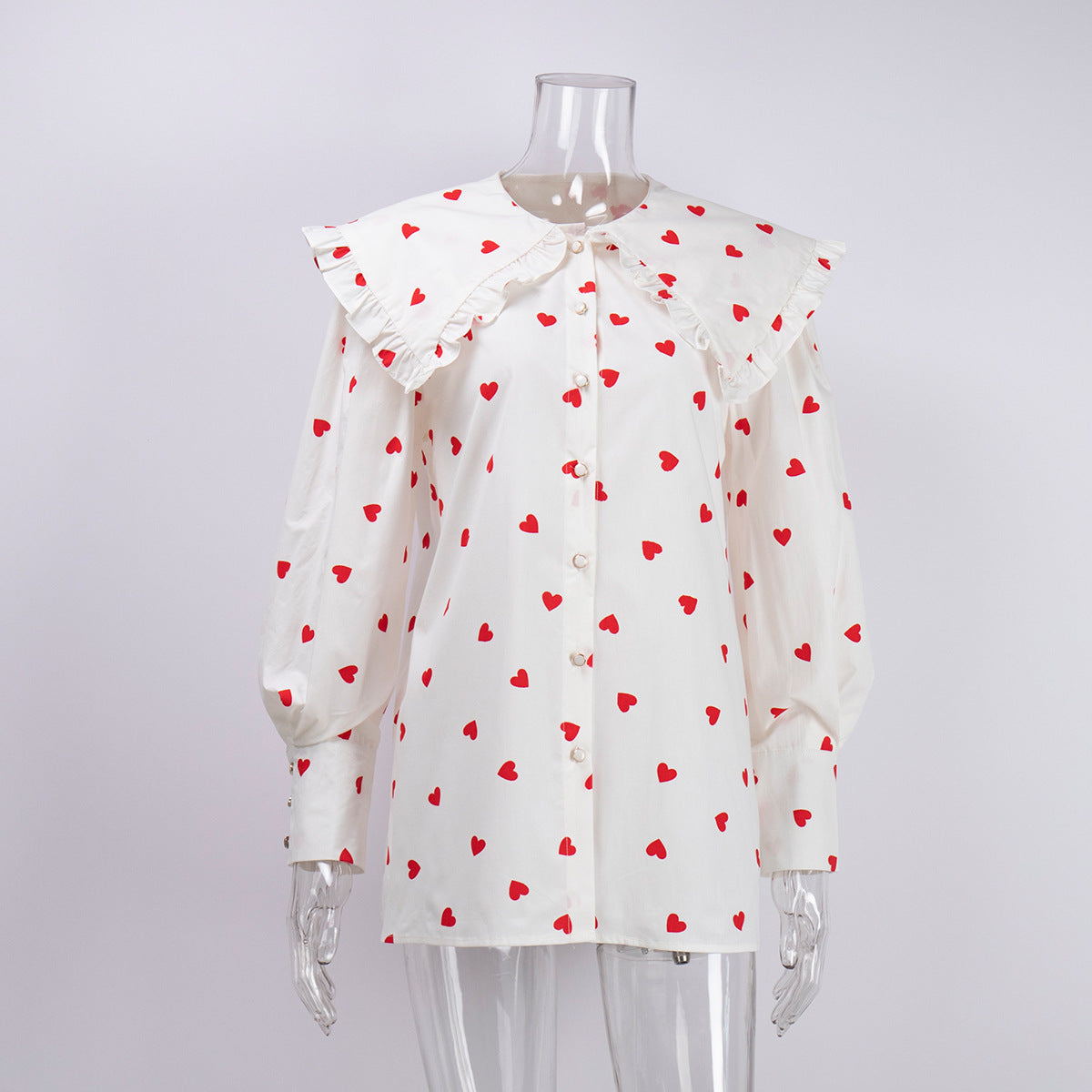 White heart-print blouse with oversized ruffle collar and button front displayed on mannequin torso against neutral background