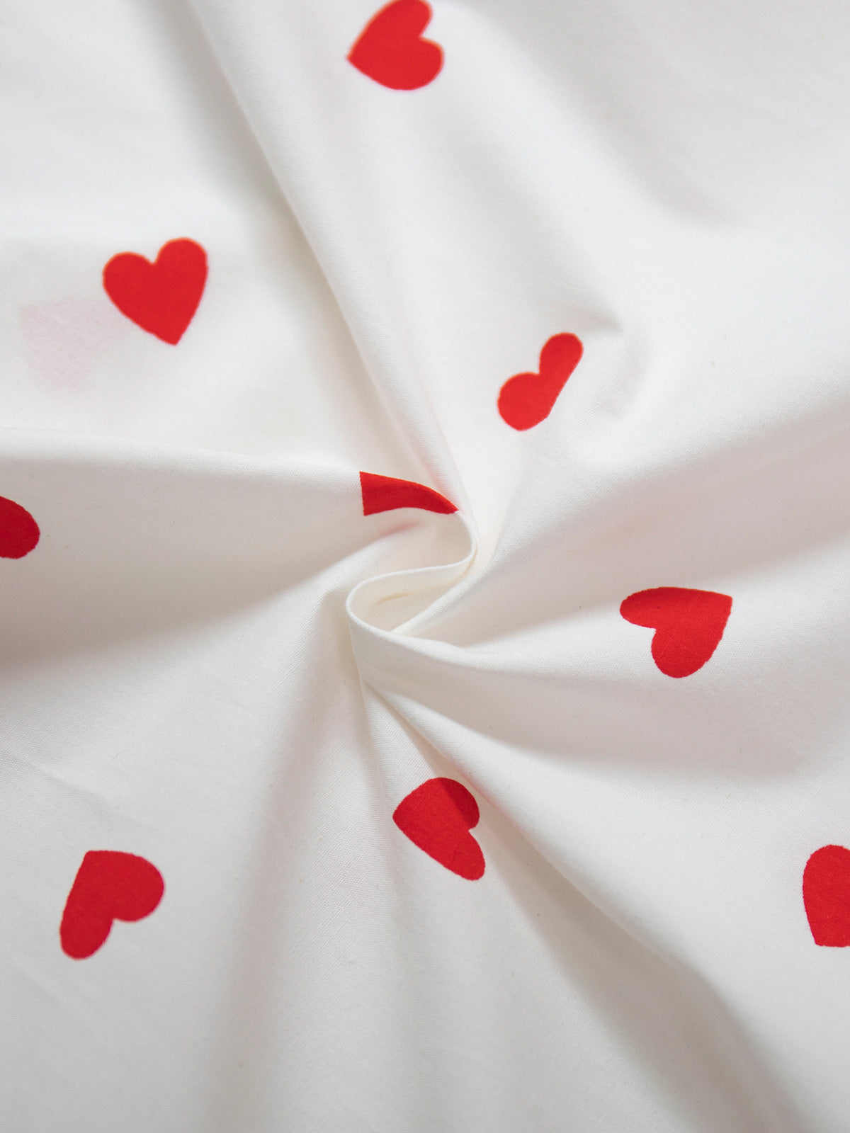 Close-up of white cotton fabric with scattered red heart print pattern showing textile texture and color contrast