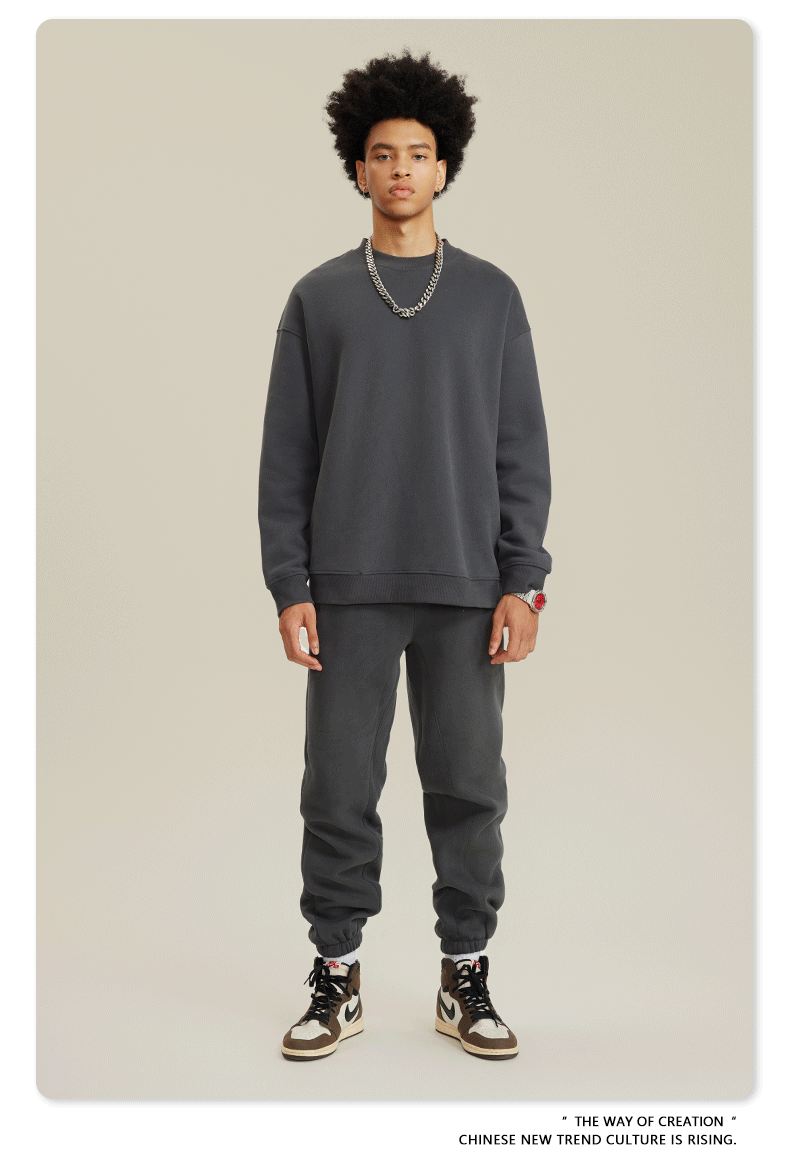 Male model wearing dark gray sweatsuit set with silver chain necklace, red watch and brown/white Jordan sneakers