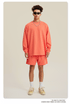 Man in coral sweatshirt and shorts set with sunglasses, chain necklace and beige sneakers