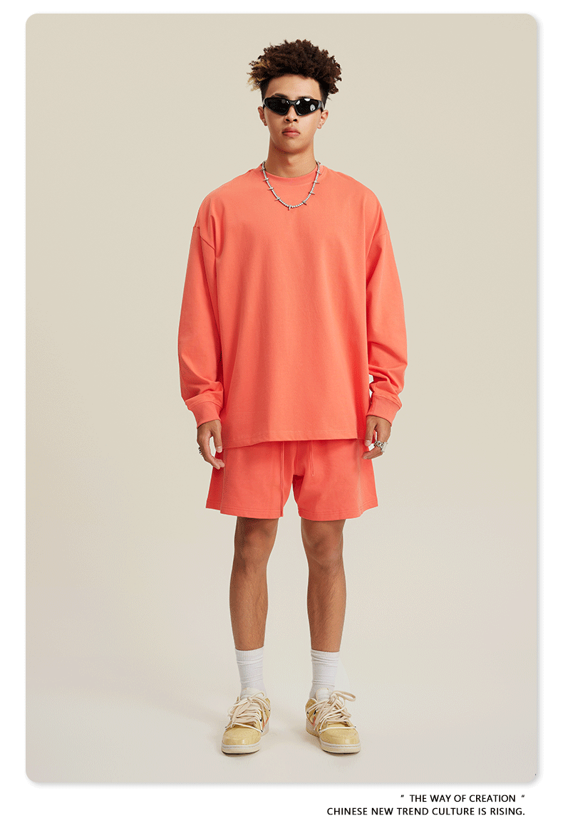 Man in coral sweatshirt and shorts set with sunglasses, chain necklace and beige sneakers