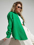 A woman wearing an emerald green textured button-down shirt with white crop top and pants, wearing sunglasses against white background