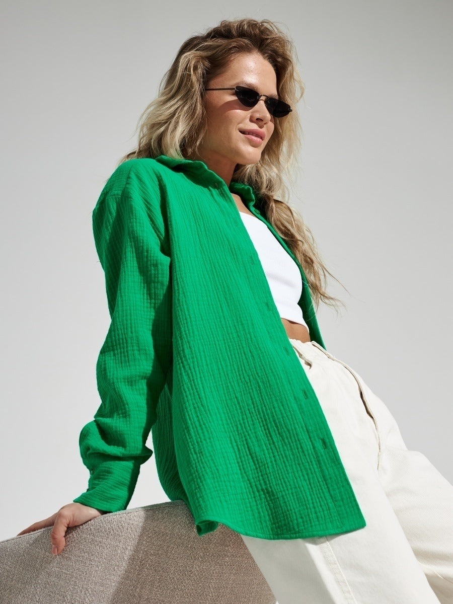 A woman wearing an emerald green textured button-down shirt with white crop top and pants, wearing sunglasses against white background