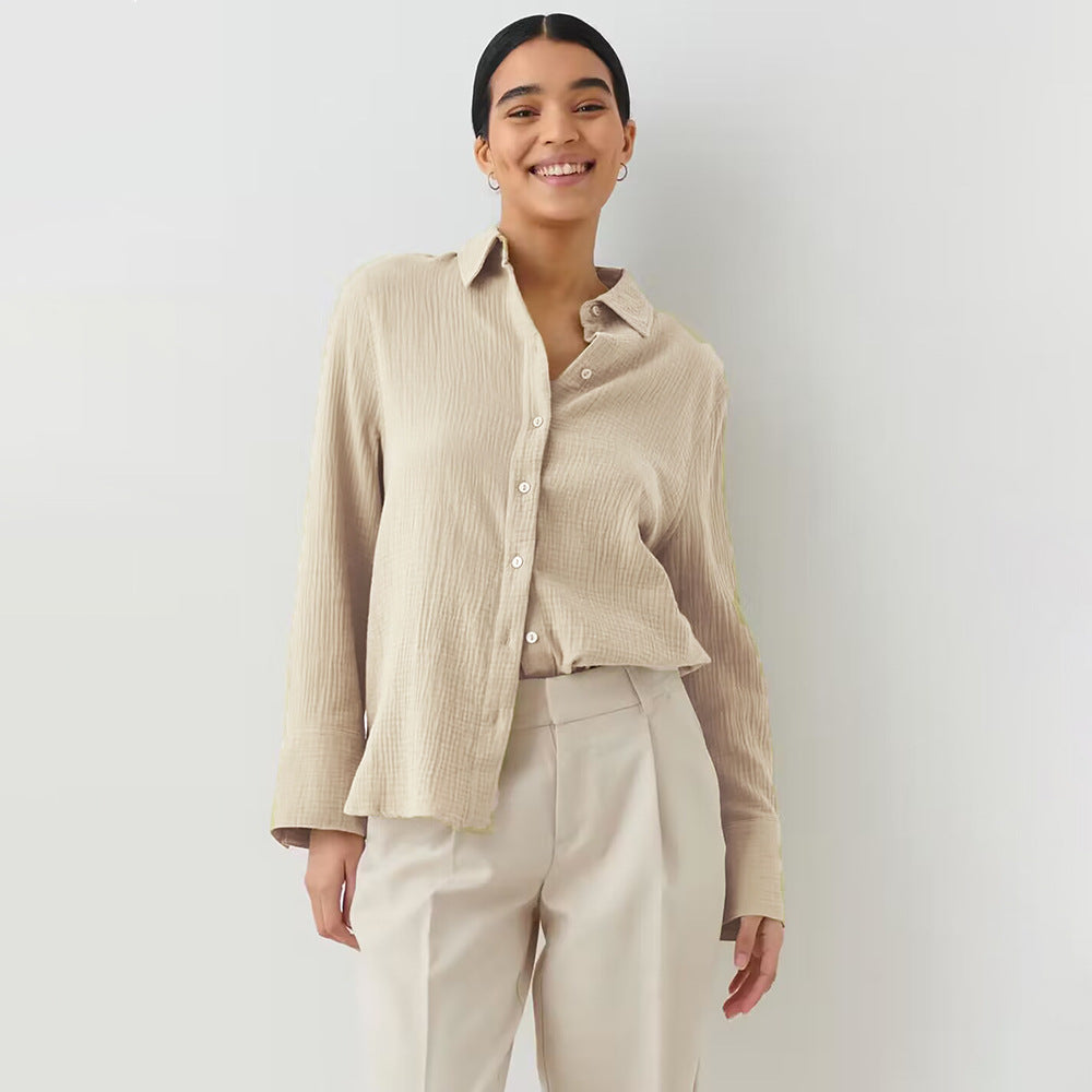 A woman wearing a beige textured button-down shirt with matching trousers, smiling broadly against white background