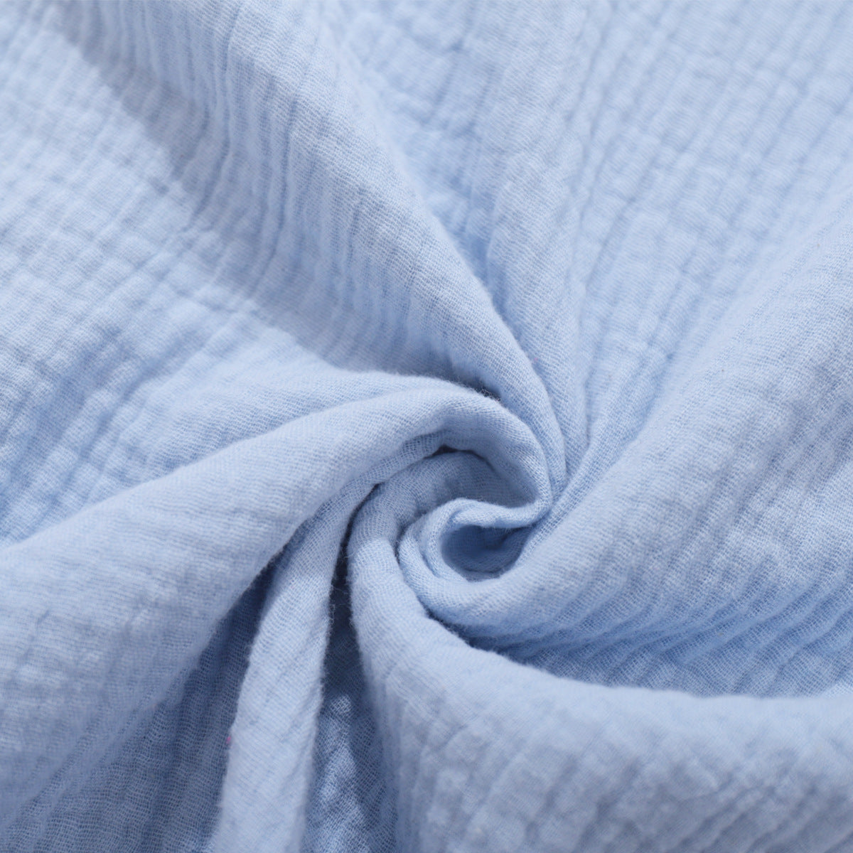A close-up of light blue textured cotton fabric showing the crinkled gauze material with natural wrinkles against light background
