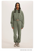 Muted Green Sweatshirt and Joggers Set – Model wears a sage green cropped hoodie and matching sweatpants with sneakers