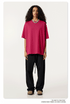 Female model wearing hot pink oversized t-shirt with black relaxed pants, silver chain necklace and beige shoes against clean white background