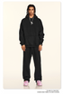 Model wearing black hoodie and sweatpants with silver necklace and pink sneakers on neutral background