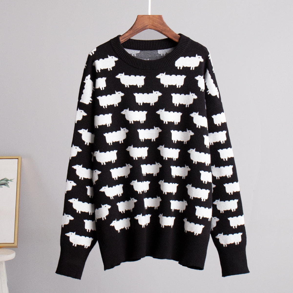 Black knit sweater with contrasting white sheep pattern on wooden hanger