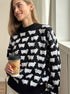 Black knit sweater with white sheep pattern print, styled with coffee cup