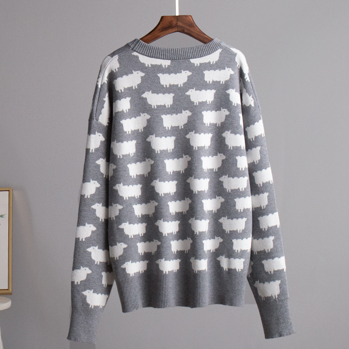 Gray knit sweater with repeating white sheep pattern, displayed on wooden hanger
