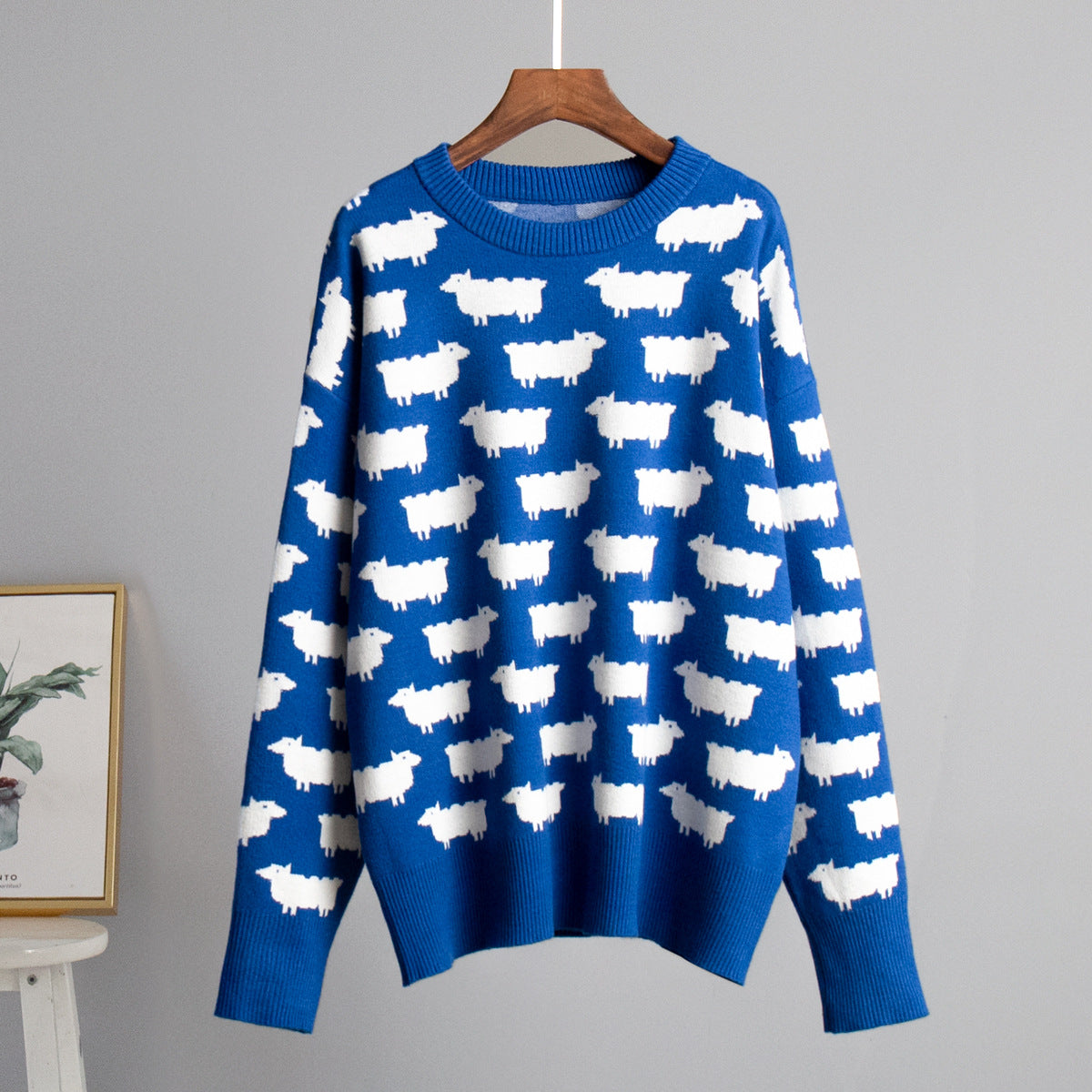 Royal blue sweater with repeating white sheep motif on wooden hanger