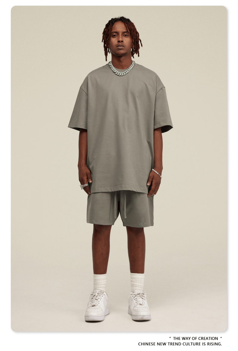 Close-up front view of man in sage green oversized T-shirt and matching shorts with silver chain necklace