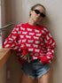 Red knit sweater with white sheep pattern worn with denim shorts and black sunglasses