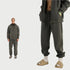 Model in dark gray hoodie opened to show bare chest, with matching sweatpants and tan slide sandals