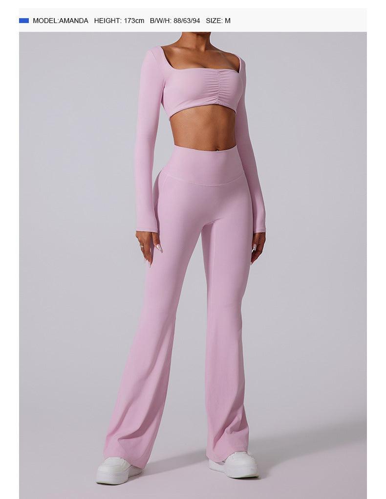 Model wearing lilac workout set featuring long-sleeve crop top and flared pants, paired with white sneakers on studio backdrop