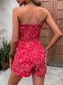 Back view of a woman in a red strapless tropical print romper, showing smocked detail on top.
