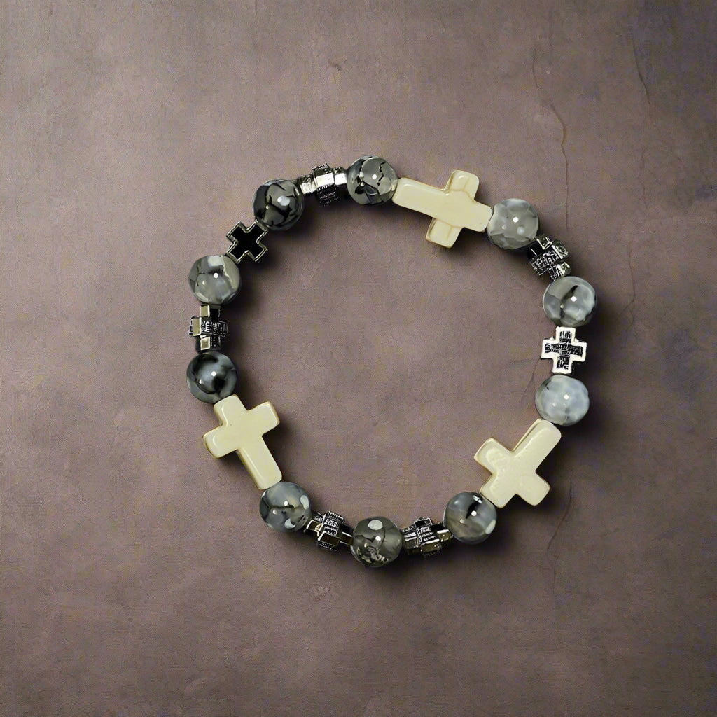 A stretch bracelet with a mix of black, gray, and white beads, featuring white cross-shaped beads and silver cross charms.