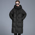 A woman wearing a black oversized quilted puffer coat with hands in pockets, black sunglasses and red lipstick, standing against gray background