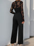 The back view of a black lace jumpsuit showing sheer floral lace sleeves and a fitted waist, styled with white heels.
