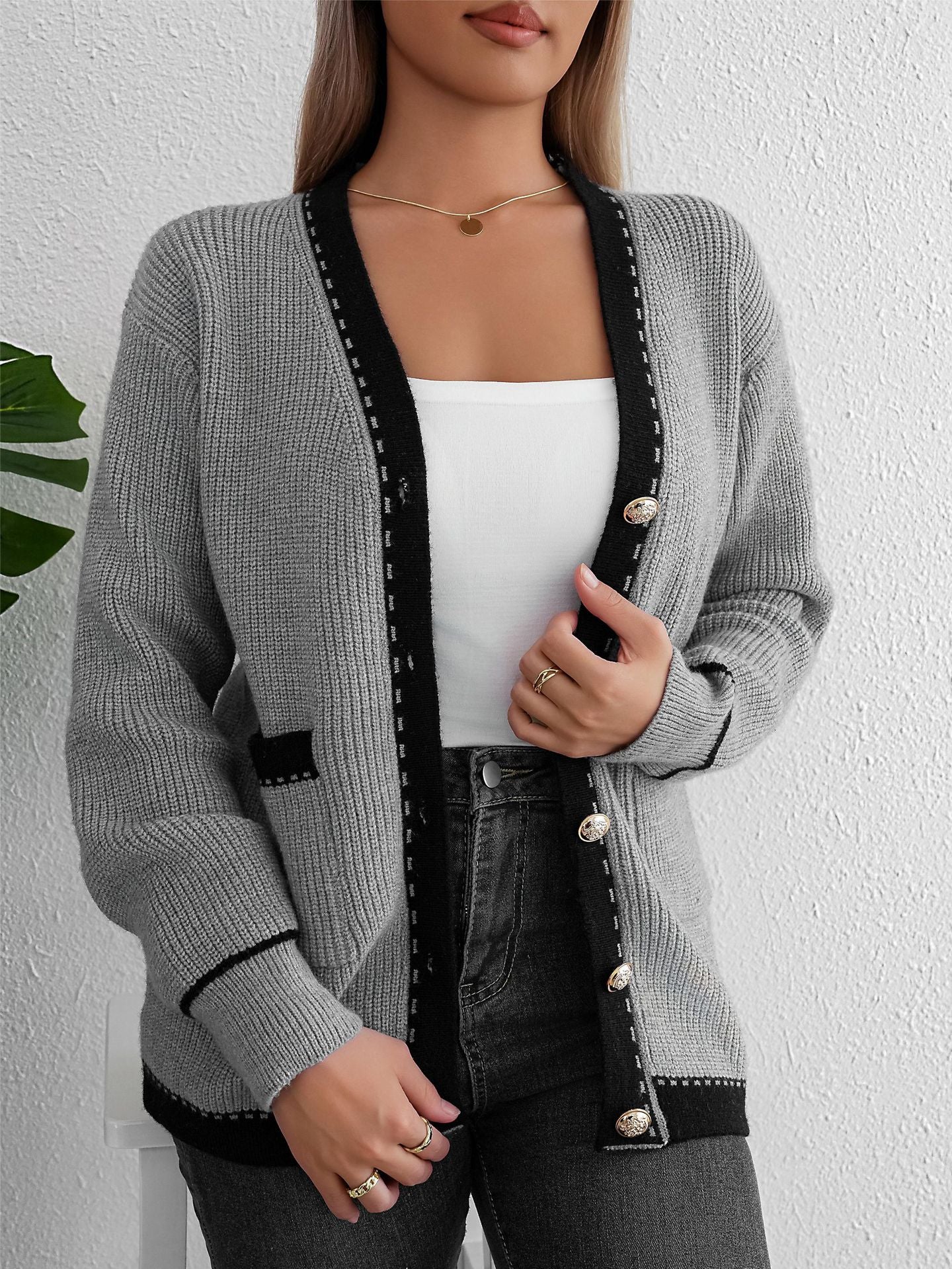 Gray knit cardigan buttoned up, showing black trim and pockets, worn with white tank and jeans