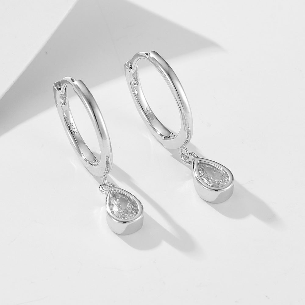 Silver 925 stamped huggie hoops with dangling teardrop cubic zirconia charms against white backdrop