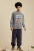 A male model wears a gray oversized "RECOLLECT" sweatshirt with a colorful print, navy sweatpants, and sneakers, posing neutrally