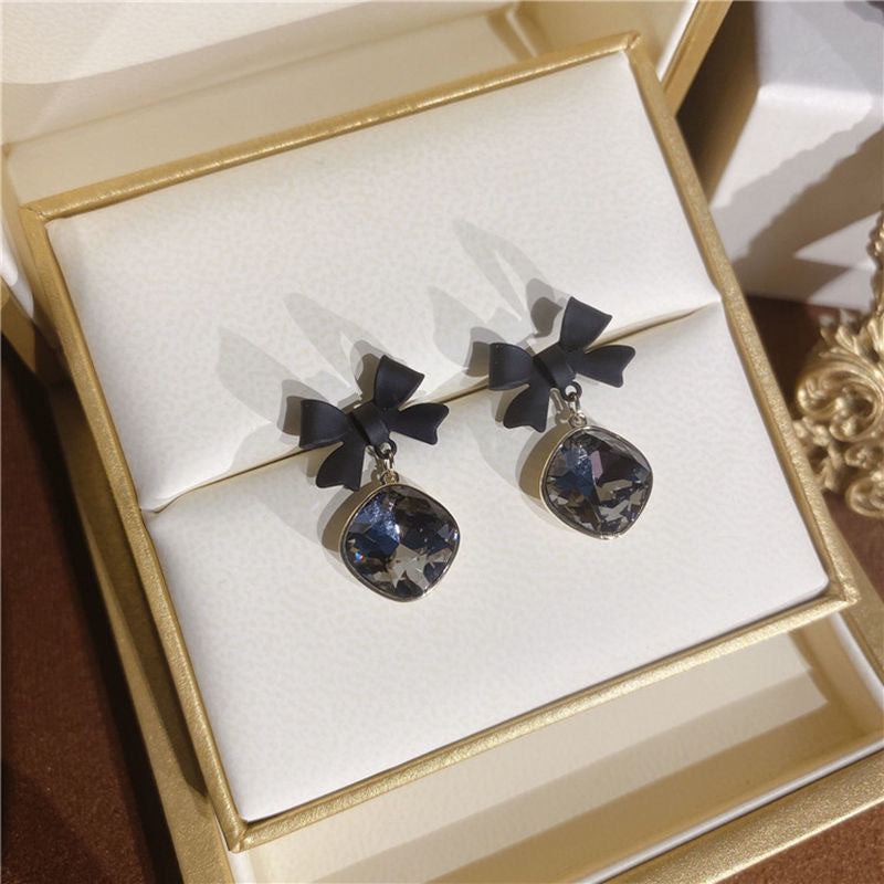 Black bow crystal earrings displayed in a gold-trimmed white jewelry box