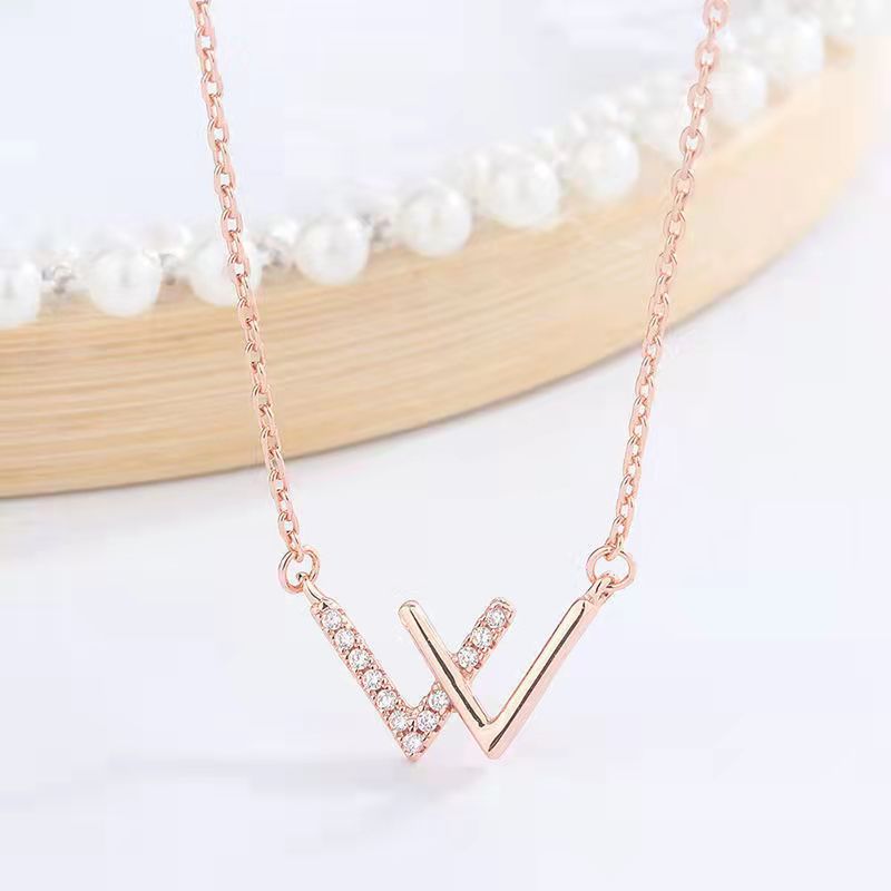 Rose gold W initial necklace with cubic zirconia detail against white background with pearl decor element