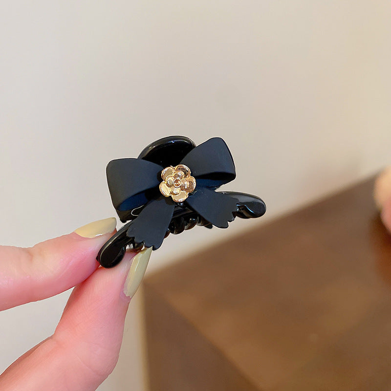 Hand holding black bow hair clip showing glossy finish