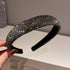 Black rhinestone headband with densely packed crystals, reflecting golden and blue sparkles, held against a neutral background.