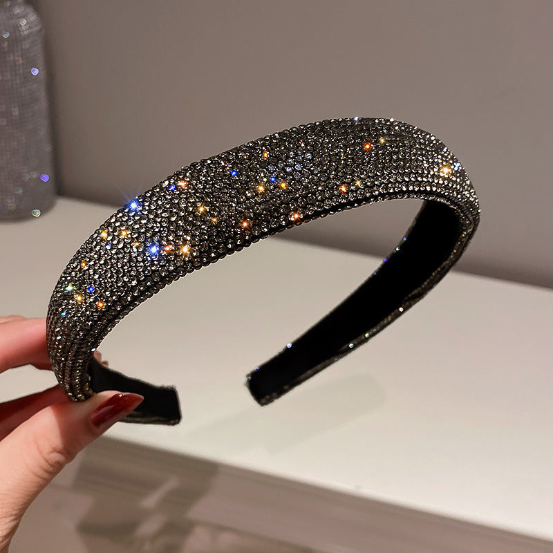 Black rhinestone headband with densely packed crystals, reflecting golden and blue sparkles, held against a neutral background.