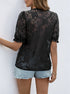 Back view of a women wearing sheer black lace blouse featuring floral embroidery and ruffled sleeves, paired with denim shorts.