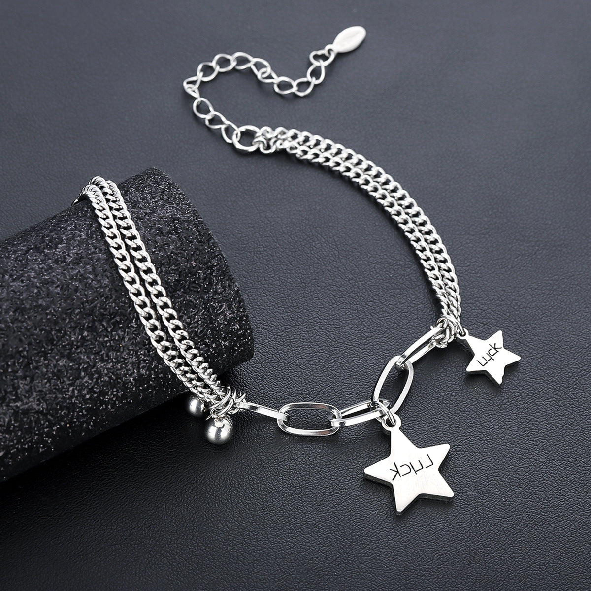 A close-up of the bracelet draped over a textured black cylindrical display, showcasing its chain-link structure, charms, and bead details.